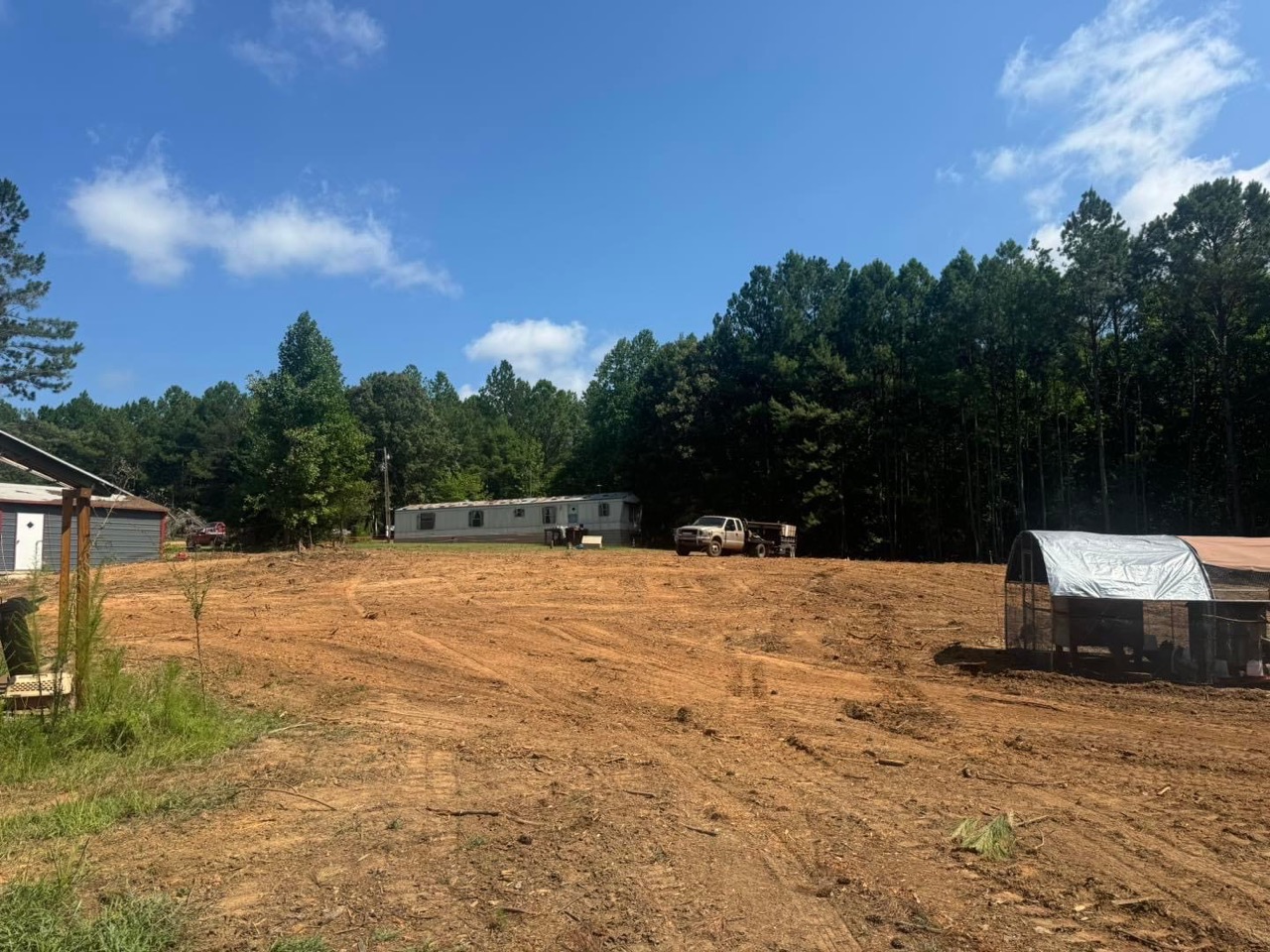 Cleared land featuring a mobile home and a parked vehicle surrounded by trees